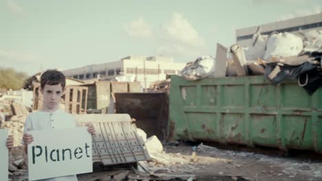 Save-the-planet.-young-kids-holding-signs-standing-next-to-huge-junkyard