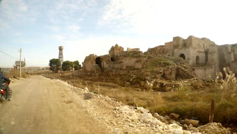 un-motociclista-paseos-a-través-de-una-calle-al-lado-de-un-castillo-medieval-en-ruinas-de-la-aldea-en-el-sureste-de-Turquía