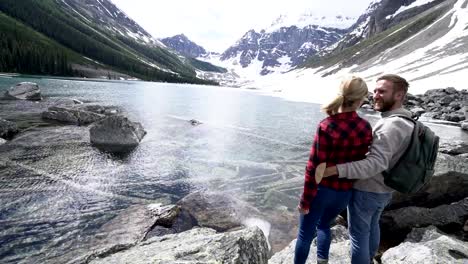 Couple-stands-by-the-lake-arms-outstretched-in-the-air