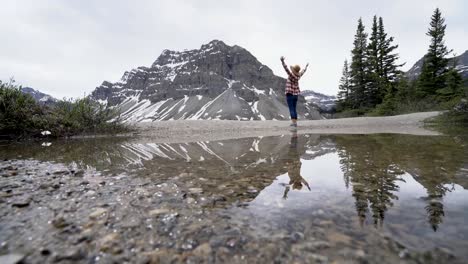 Young-woman-stands-by-beautiful-mountain-lake-scenery-with-her-arms-wide-open