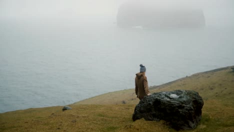 Back-view-of-young-woman-walking-on-the-shore-of-the-sea-and-thinking,-exploring-the-nature-of-Iceland