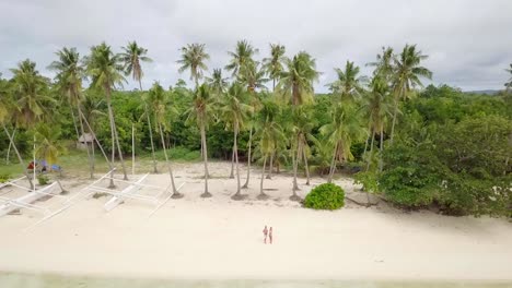 Young-couple-playing-with-drone,-waving-hands-to-the-flying-helicopter.-People-fun-new-technology-vacations-concept.-Shot-on-tropical-beach-in-the-Philippines,-4K-resolution