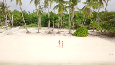 Young-couple-playing-with-drone,-waving-hands-to-the-flying-helicopter.-People-fun-new-technology-vacations-concept.-Shot-on-tropical-beach-in-the-Philippines,-4K-resolution