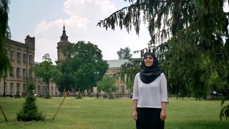 Joven-hermosa-mujer-musulmana-en-hijab-es-de-pie-y-sonriente-durante-el-día,-disfrutando-de-clima,-basándose-en-antecedentes,-concepto-de-epoca