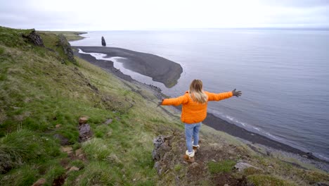 Young-woman-arms-outstretched-at-Hvitserkur-basalt-stack-along-the-eastern-shore-of-the-Vatnsnes-peninsula,-in-northwest-Iceland.-People-travel-lifestyles-concept