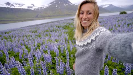 Selfie-portrait-of-tourist-female-in-Iceland-in-the-middle-of-Lupine-purple-flowers,-smiling-hair-in-wind,-wool-seater