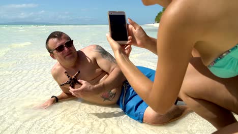 A-woman-is-taking-pictures-of-a-man-with-a-starfish-on-a-smartphone