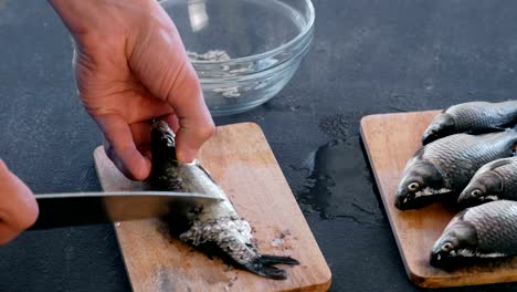 Man-reinigt-Karpfen-von-der-Waage-auf-Holzbrett.-Close-up-Hände.-Kochen-einen-Fisch.