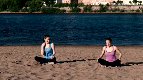 Zwei-Frauen-Yoga-am-Strand-am-Fluss-in-der-Stadt-zu-tun-und-reden.-Schöne-Aussicht.