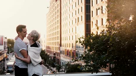 Beautiful-Hispanic-man-and-Caucasian-woman-standing-and-hugging,-holding-hands-on-New-York-City-summer-sunset-bridge