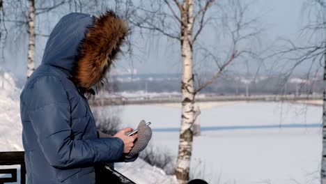 Mujer-irreconocible-en-azul-chaqueta-escribe-mensajes-en-su-teléfono-celular-en-el-parque-de-invierno.-Vista-lateral