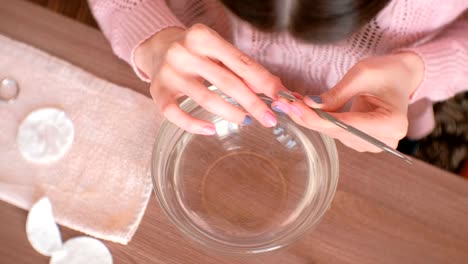 Frau-entfernen-Nagelhaut-mit-Drücker.-Macht-Maniküre-selbst.-Close-up-Hände.-Ansicht-von-oben.-Werkzeuge-auf-Tisch.