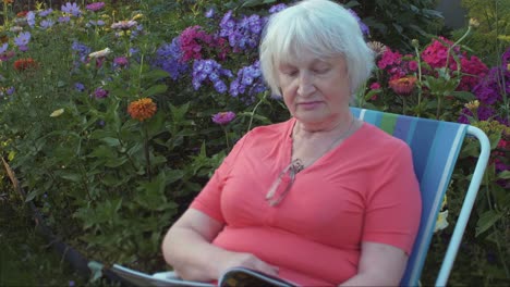 Senior-mujer-leyendo-revista-en-jardín-con-flores-al-aire-libre