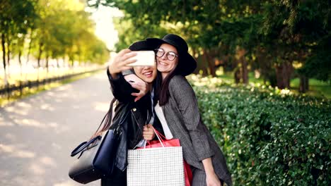 Aufgeregte-Freundinnen-nehmen-Selfie-mit-Smartphone-und-Einkaufstaschen-mit-Käufen-an-sonnigen-Herbsttag-hält.-Moderne-Technologie-und-Jugend-Konzept.