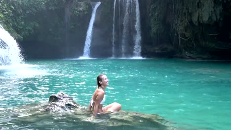 Young-woman-contemplating-a-beautiful-waterfall-on-the-Cebu-Island-in-the-Philippines.-People-travel-nature-loving-concept.-One-person-only-enjoying-outdoors-and-tranquillity-in-a-peaceful-environment