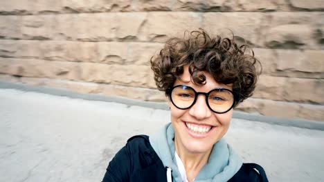 Point-of-view-shot-of-carefree-young-lady-with-short-hair-and-glasses-looking-at-camera-and-laughing-turning-around-in-the-street-having-fun-on-autumn-day.