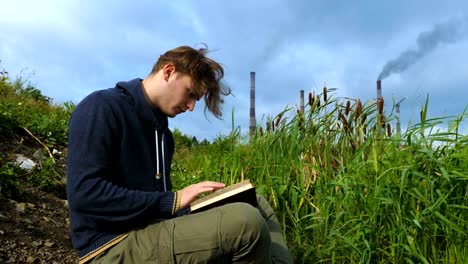 Ein-junger-Mann-sitzt-am-Fluss-und-liest-ein-Buch.