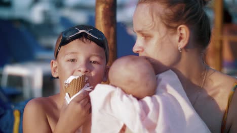 Mutter-mit-Baby-und-älteren-Sohn-am-Strand.-Junge,-Eis-essen