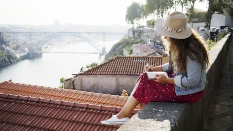 Young-lady-with-notebook-and-pen-sitting-near-roofs