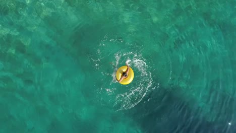 Aerial-view-of-woman-spinning-with-inflatable-on-Atokos-island,-Greece.