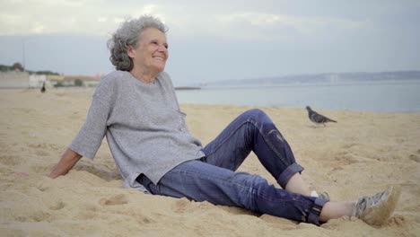 Schöne-ältere-Frau-auf-Sand-sitzen-und-lachen.