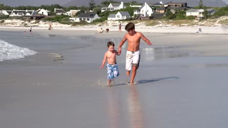 2-young-boys-running-towards-camera-on-beach,-Cape-Town