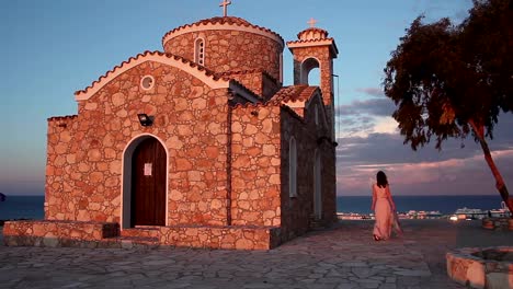 Hermosa-mujer-griega-a-cerca-de-la-antigua-iglesia,-con-vista-al-espectacular