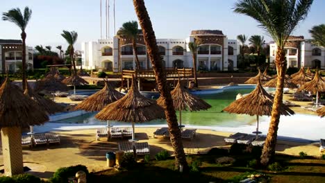 Sunny-Hotel-Resort-with-Blue-Pool,-Palm-Trees-and-Sunbeds-in-Egypt