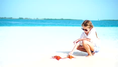 Entzückende-kleine-Mädchen-mit-riesigen-roten-Seestern-auf-weißen-leeren-Strand