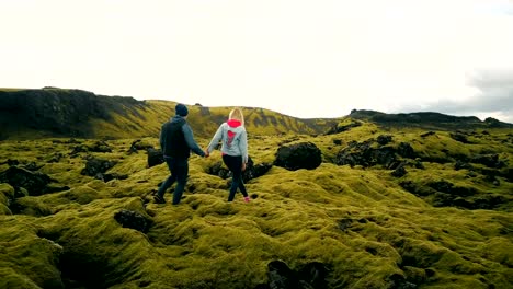 Aerial-view-of-couple-walking-through-the-lava-fields-in-iceland.-Man-and-woman-sit-on-the-rock,-enjoying-the-landscape