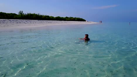 v04195-Aerial-flying-drone-view-of-Maldives-white-sandy-beach-2-people-young-couple-man-woman-swimming-splashing-underwater-on-sunny-tropical-paradise-island-with-aqua-blue-sky-sea-water-ocean-4k