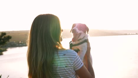 Young-attractive-woman-playing-with-a-dog-Jack-Russell-in-the-meadow-at-sunset-with-sea-background.-slow-motion