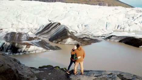 Junge-schöne-Paar-stehen-am-Ufer-des-Sees-im-Vatnajökull-Eis-Lagune-in-Island-und-auf-der-Suche-auf-Gletschern