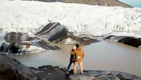 Young-beautiful-couple-standing-on-the-shore-of-the-lake-in-Vatnajokull-ice-lagoon-in-Iceland-and-looking-on-glaciers