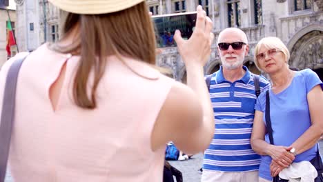 Daughter-taking-photo-of-her-senior-parents-on-vacation-trip-in-central-square-of-Brussels,-Belgium