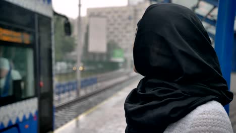 Young-muslim-woman-in-hijab-is-watching-how-train-is-coming,-raining,-religion-concept,-urban-concept