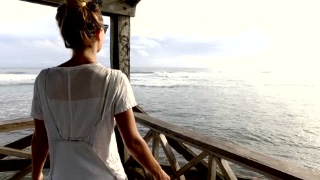 Young-woman-enjoying-sea-breeze-from-wooden-pier-over-sea-arms-outstretched