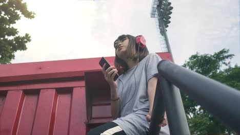 Schöne-junge-asiatische-Frau-anhören-von-Musik-auf-einem-Smartphone-in-der-Stadt.-Junge-asiatische-Frau,-entspannende-Musik-hören-auf-der-Straße.