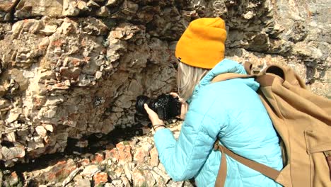 Un-fotógrafo-de-la-chica-rubia-en-un-sombrero-toma-una-foto-en-una-pose-extraña-en-su-cámara-digital-con-un-fondo-de-rocas-en-el-Cáucaso