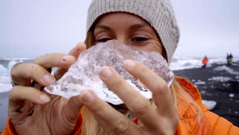 Turismo-de-mujer-de-pie-en-la-playa-de-arena-negra-en-la-pieza-de-sujeción-de-Islandia-de-hielo-en-la-mano-en-la-playa-del-diamante-cerca-de-Jokulsarlon