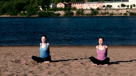 Zwei-Frau-stretching-Yoga-am-Strand-am-Fluss-in-der-Stadt.-Blick-auf-die-schöne-Stadt.-Meditation-Pose.