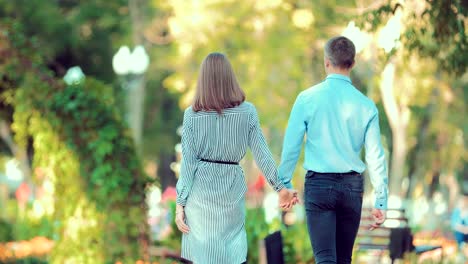 Young-couple-walk-through-a-city-park-together-heading-away-from-the-camera