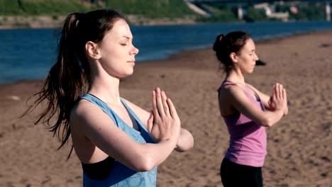 Zwei-Frau-stretching-Yoga-stehen-am-Strand-am-Fluss-in-der-Stadt.-Blick-auf-die-schöne-Stadt.-Namaste-Pose.