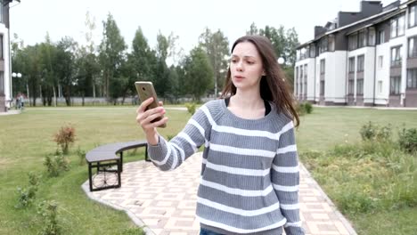 Beautiful-brunette-woman-blogger-talk-a-video-chat-on-mobile-phone-walking-near-the-home.