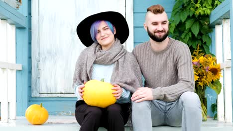 Young-woman-and-man,-family,-sitting-on-porch-of-village-house-with-pumpkins.