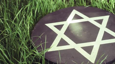 White-Star-Of-David-auf-einem-schwarzen-Stein-Runden-auf-einem-Rasen-Hintergrund,-360-Grad-Drehung.