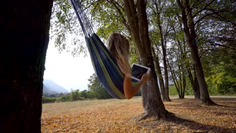 Young-woman-on-hammock-at-sunset-reading-on-digital-tablet-using-mobile-apps-on-wireless-technology.-People-travel-modern-life-concept