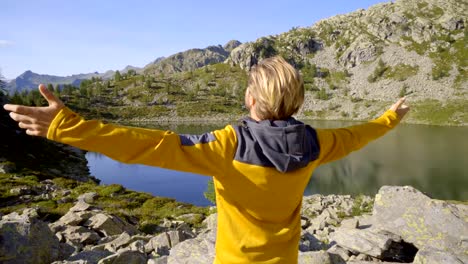 Junger-Mann-Wanderer-unterwegs-im-Sommer-durch-atemberaubende-Alpensee-Arme-ausgestreckt-feiern-persönliches-Ziel.-Junger-Mann-stehend-in-der-Natur,-die-Arme-weit-öffnen