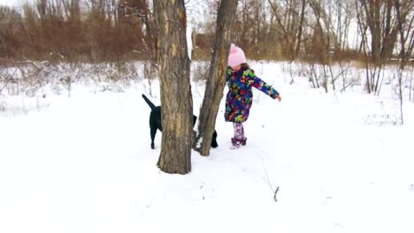 Kleines-Mädchen-spielt-mit-ihren-schwarzen-Labrador-auf-Schnee