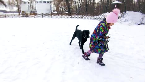 Kleines-Mädchen-spielt-mit-ihren-schwarzen-Labrador-auf-Schnee